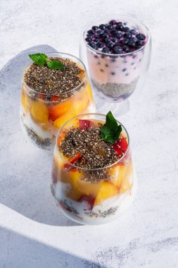 Parlak gri beton arka planda üç bardak Chia tohumu pudingi. Tatlı yaban mersini, meyve kahvaltısı. Modaya uygun organik krema. Doğal besin maddeleriyle vejetaryen atıştırması. Durgun hayat