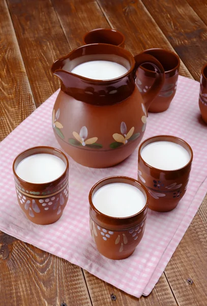 Kil sürahi ve üç bardak süt bir ahşap tablo.