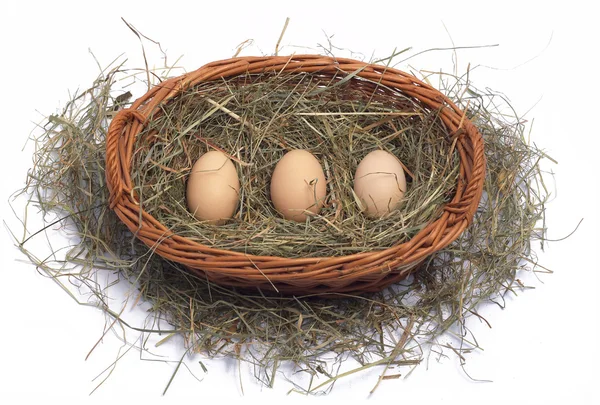 Three organic eggs in a wicker basket on the hay — Zdjęcie stockowe
