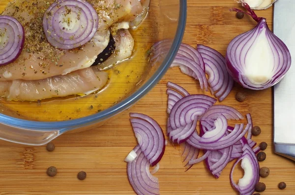 Raw chicken with onion in casserole dish 