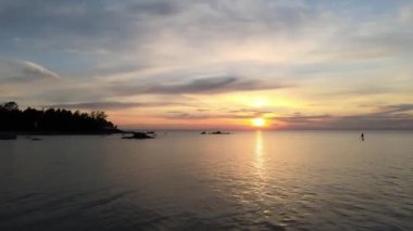 Gün batımında güneşe karşı sup sörfçüsü silueti