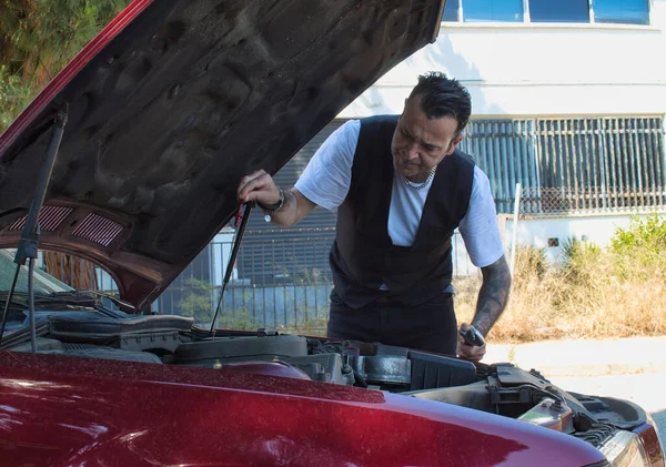 Olgun bir adam yol kenarındaki aletlerle araba motorunu tamir ediyor.