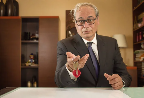 İş adamı kendinden emin ve neşeli bir ifadeyle evin anahtarlarını oynuyor ve gösteriyor