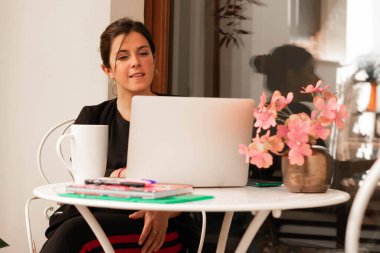 Toplantıda gülümseyen dizüstü bilgisayarla evde çalışan genç bir kadının yatay görüntüsü.