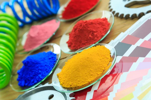 Toz boya kaplı metal parçaları ile cam tabakta ve renk tablosu yığını.