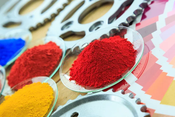 Toz boya kaplı metal parçaları ile cam tabakta ve renk tablosu yığını.