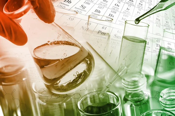 Laboratorní sklo, zkumavky a baněk v laboratoři s chemických rovnic a Periodická tabulka pozadím. — Stock fotografie