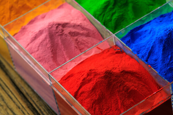 The pile of powder coating in plastic box, on wooden background.