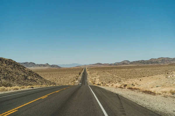 Pustynna droga autostrady prowadząca na horyzont przed błękitnym niebem i górami — Zdjęcie stockowe