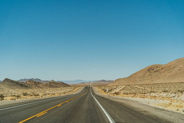 Desert highway road leading to the horizon against clear blue sky and mountains