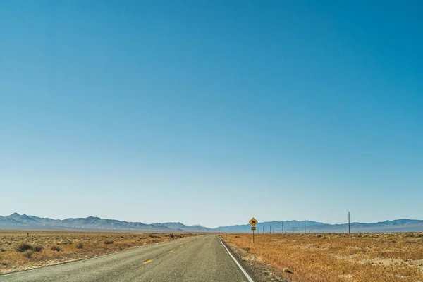 Pustynna droga autostrady prowadząca na horyzont przed błękitnym niebem i górami — Zdjęcie stockowe