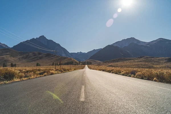 Two lane road in the arid Sierra Nevadas leading to mountains against blue sky — Stock Photo, Image