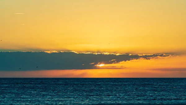 Az epikus, színes naplemente vörös és narancssárga felhőket világít meg a kék vizek felett. — Stock Fotó