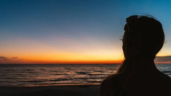 Woman watches sunset over ocean beach in silhouette from behind — Stock Photo, Image