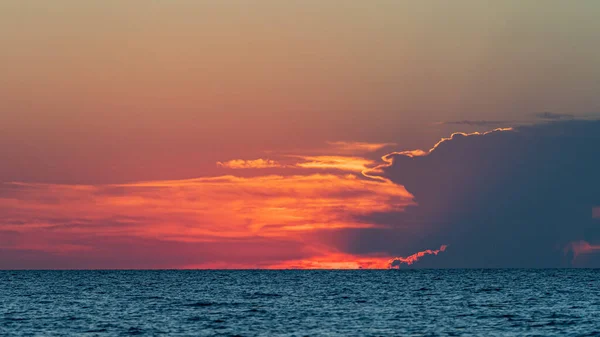 Epicki kolorowy zachód słońca oświetla chmury czerwone i pomarańczowe nad błękitnymi wodami — Zdjęcie stockowe