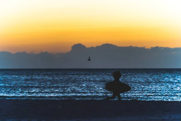Young man runs along beach in silhouette with boogie board at sunset. — Stock Photo, Image