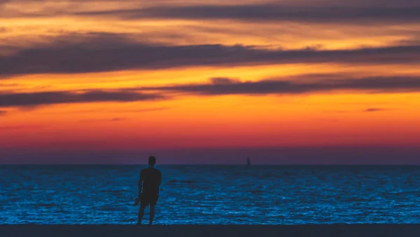 Uomo in vacanza in spiaggia, silhouette tramonto nuvole vibranti e cielo — Foto Stock