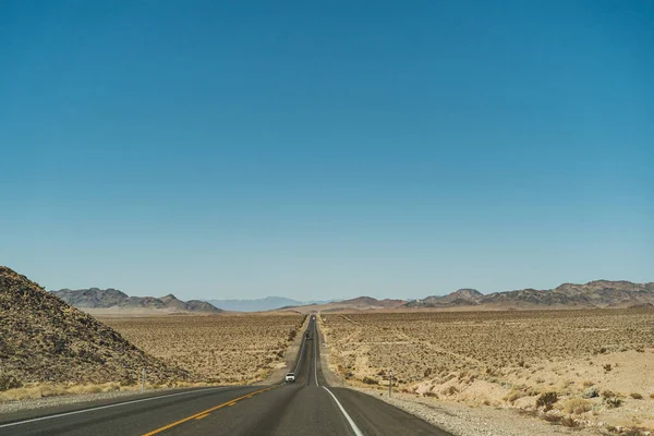 Woestijn snelweg die leidt naar de horizon tegen helder blauwe lucht en bergen — Stockfoto