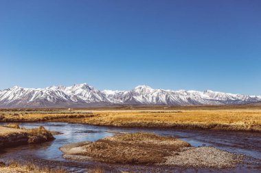 River runs though Arid plain against Sierra Nevada Mountains blue sky  clipart