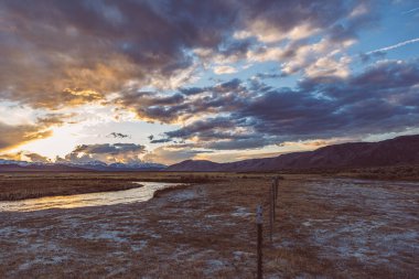 Nehir, Arid ovasında dramatik günbatımı gökyüzüne ve dağlara karşı akar.