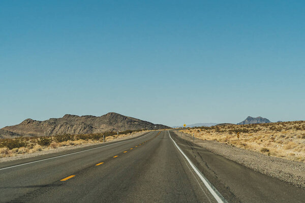 Desert highway road leading to the horizon against clear blue sky and mountains