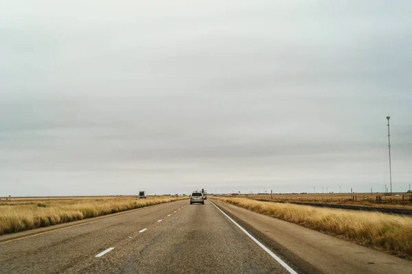 Μονό αυτοκίνητο σε άδειο αυτοκινητόδρομο στις αμερικανικές πεδιάδες κατά συννεφιασμένο ουρανό — Φωτογραφία Αρχείου