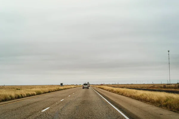 Singola auto in autostrada vuota nelle pianure americane contro cielo coperto — Foto Stock