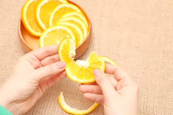 Fruit in een houten kom in haar hand heen en weer geslingerd oranje, klaar voor consum, vrucht van sappige rijpe oranje in een houten plaat blootgesteld aan mooie illustraties van Oranje, haar hand houdt het segment van Oranje ontleend aan een houten plaat, op de achtergrond van jute spinnin — Stockfoto