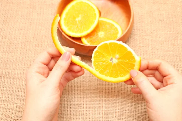 Fruit in een houten kom in haar hand heen en weer geslingerd oranje, klaar voor consum, vrucht van sappige rijpe oranje in een houten plaat blootgesteld aan mooie illustraties van Oranje, haar hand houdt het segment van Oranje ontleend aan een houten plaat, op de achtergrond van jute spinnin — Stockfoto