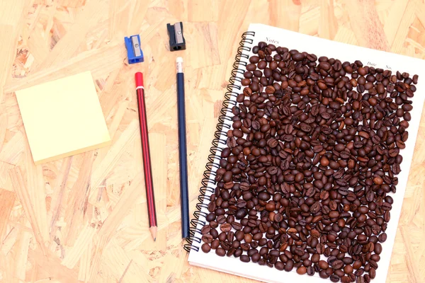 Kaffeebohnen auf einem Notizbuch mit einer Reihe von Büros — Stockfoto
