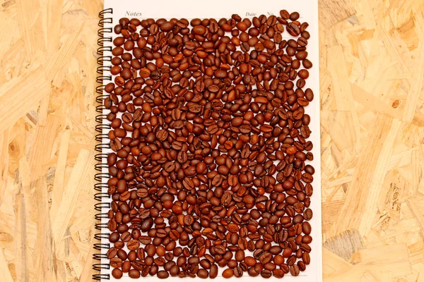Grains de café torréfiés sur un carnet, arabica — Photo