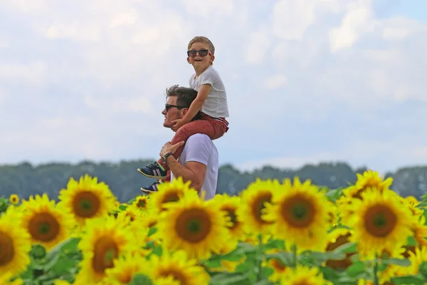 Glücklicher, fröhlicher Vater mit seinem niedlichen, klugen, gutmütigen Sohn im Feld der blühenden Sonnenblume — Stockfoto