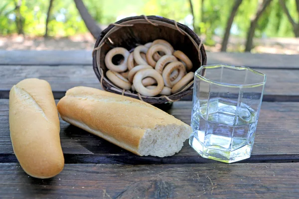 Ποτήρι νερό, ψωμί, χωρισμένο στα δύο, με ψωμί-δαχτυλίδια στην καρτέλα — Φωτογραφία Αρχείου