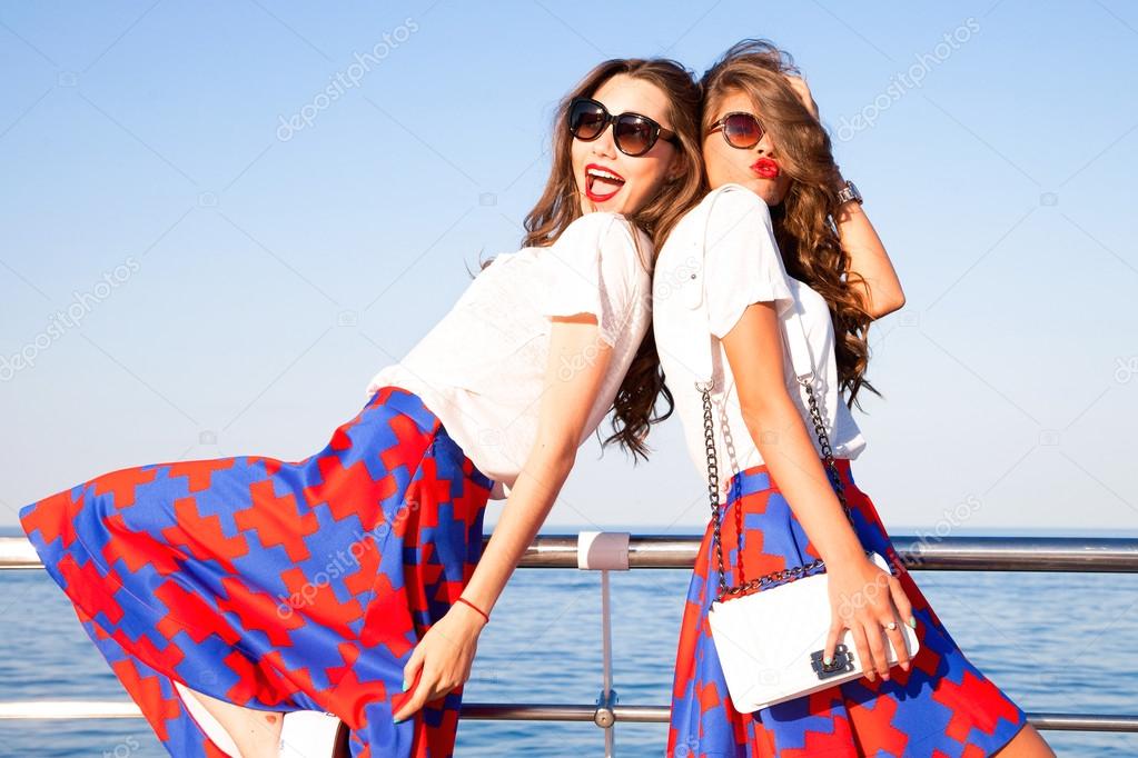 Outdoor lifestyle portrait of two best friends hipster girls wearing stylish bright outfits, denim shorts and glasses, going crazy and having great time together.Laughing and send kiss,lovely friends