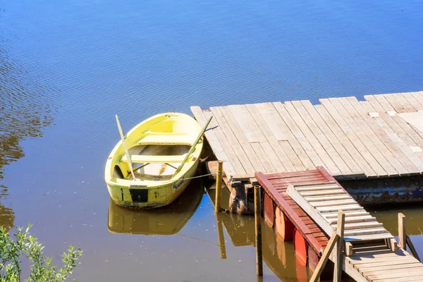 A boat with oars stands at a wooden pier in the water on a sunny summer day without people