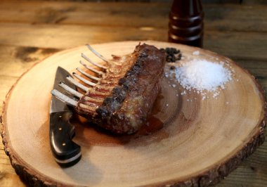 Fransız Rack. Kuzu kaburgaları ahşap arka planda ızgara. Küçük bıçak, tuz ve biberle birlikte..