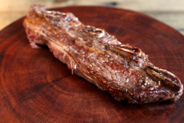 Assado de Tira. Izgarada kemikle ızgara et. Öküzün kaburga kısmında sığır eti. Ahşap arka planda.