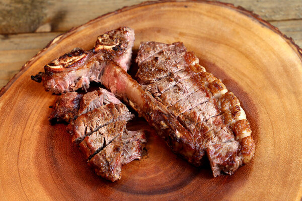 Steak grilled on the grill with bone and two types of meat. On wooden background.