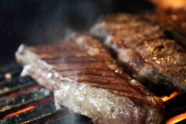 Picanha ızgaranın üstünde ızgara izleriyle yaklaş. Arka planda parlayan kömür var..