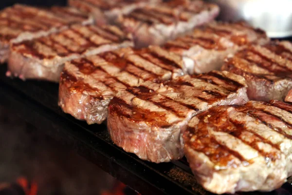 Izgarada ızgara anço bifteği ve arka planda parlayan kömür. Bir sürü biftek sıraya dizildi..
