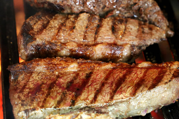 Beautiful juicy Picanha close up with grill marks on top of the grill with glowing coal on the background.