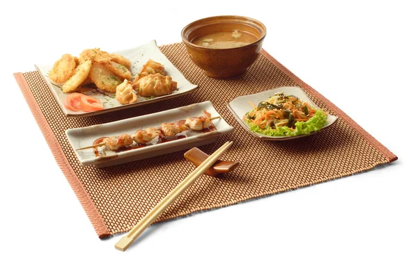 Asiatiska affärslunch med sallad, gedze, tempura, misosoppa, kani sarada, yakitori tori och pinnar på mattor över vit bakgrund — Stockfoto