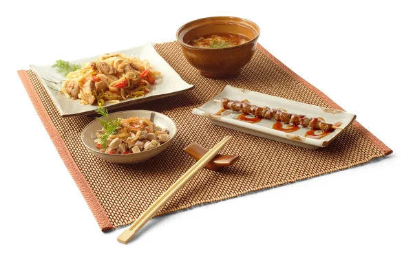 Almuerzo de negocios asiático con ensalada de carne, sopa con champiñones, udon con cerdo y verduras, yakitori y palillos en la estera sobre fondo blanco — Foto de Stock