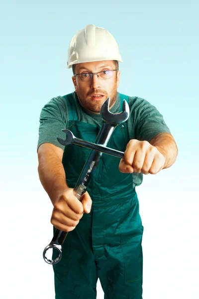 Überraschter abergläubischer Arbeiter mit Helm, Brille und Overall verteidigt sich mit Kreuz gegen Schraubenschlüssel — Stockfoto