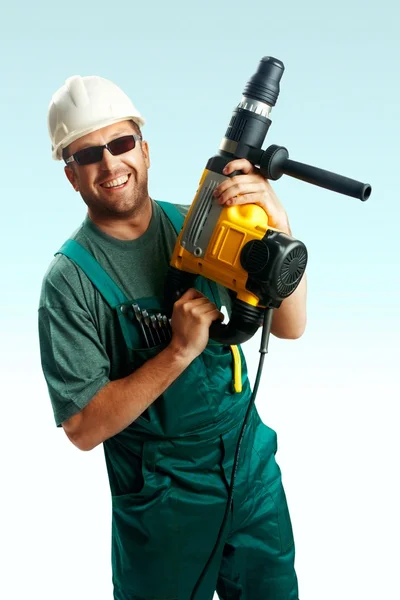 Lächelnder Arbeiter mit Helm, schwarzer Brille und Overalls hält Perforator in den Händen vor weißem Hintergrund — Stockfoto