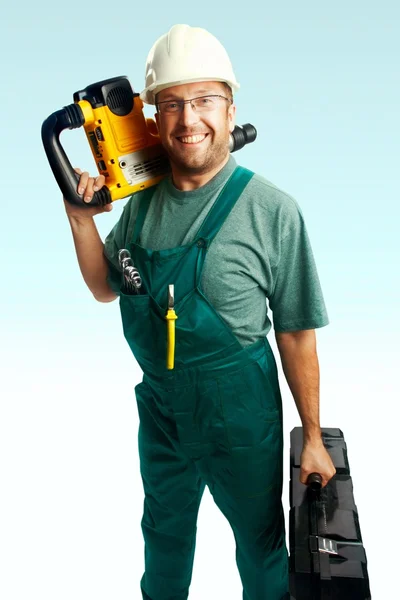 Lächelnder Arbeiter mit Helm, Brille und Overalls halten Perforator auf der Schulter und großen schwarzen Koffer in der Hand vor weißem Hintergrund — Stockfoto