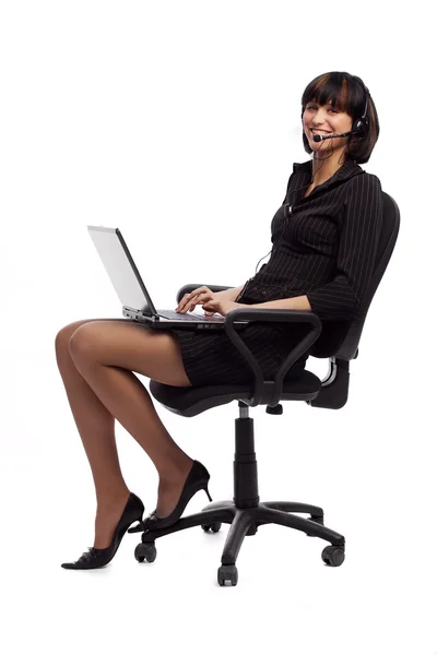 Rindo mulher morena em vestido escuro sentado na cadeira do escritório e segurando laptop sobre fundo branco — Fotografia de Stock