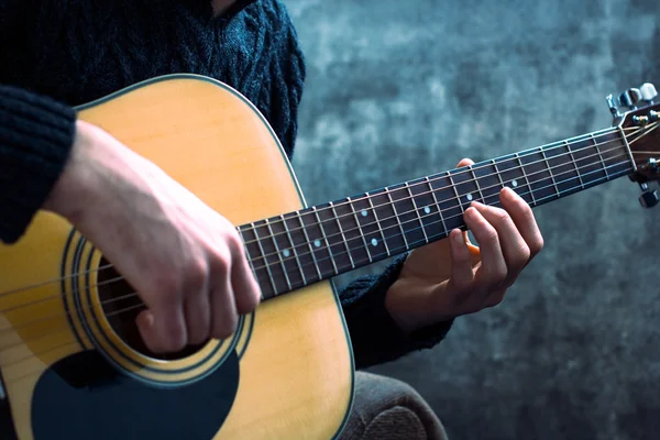 stock image young man playing an acoustic guitar on the background of a concrete wall