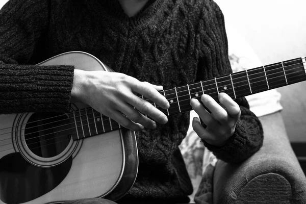 Jovem tocando uma guitarra acústica no fundo de uma parede de concreto — Fotografia de Stock