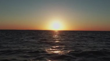 Hava aracı atışı. Denizin üzerinde şafak. Soluk sarı güneş. Sakin hava.